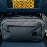 A compact travel backpack placed under an airplane seat, demonstrating the correct size for airline personal item requirements