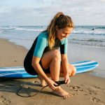 A beginner surfer attaching a surfboard leash to their ankle before paddling out into small waves