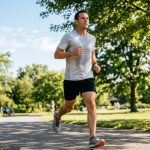 A man wearing a breathable light-grey polyester workout t-shirt while running outdoors on a sunny summer day