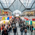 Thousands of visitors and exhibitors filling the grand halls of Messe Frankfurt during the opening days of the Frankfurt Book Fair 2026, with colorful publisher stands stretching across multiple exhibition floors