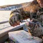 Cold bare hands struggling to tie a fishing knot on a freezing misty lake.