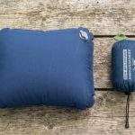 A backpacker holding a compressed camping pillow next to a tent.