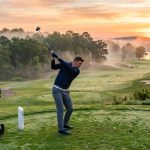 A golfer swinging on a foggy green course wearing a performance pullover jacket.