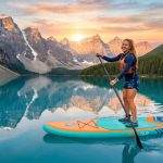 Paddler on an inflatable stand-up paddleboard on a calm lake.