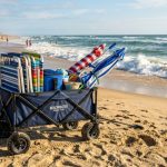 Heavy-duty foldable beach wagon loaded with gear on coastal sand.