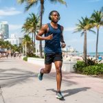 A male runner wearing over-ear headphones on a sunny Florida sidewalk.