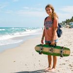 Teenager holding an affordable skateboard with a carrying handle at a Florida park.